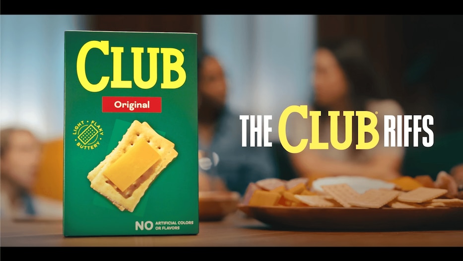 Opening shot of a club crackers originals box with blurred people in the background sitting around the box
